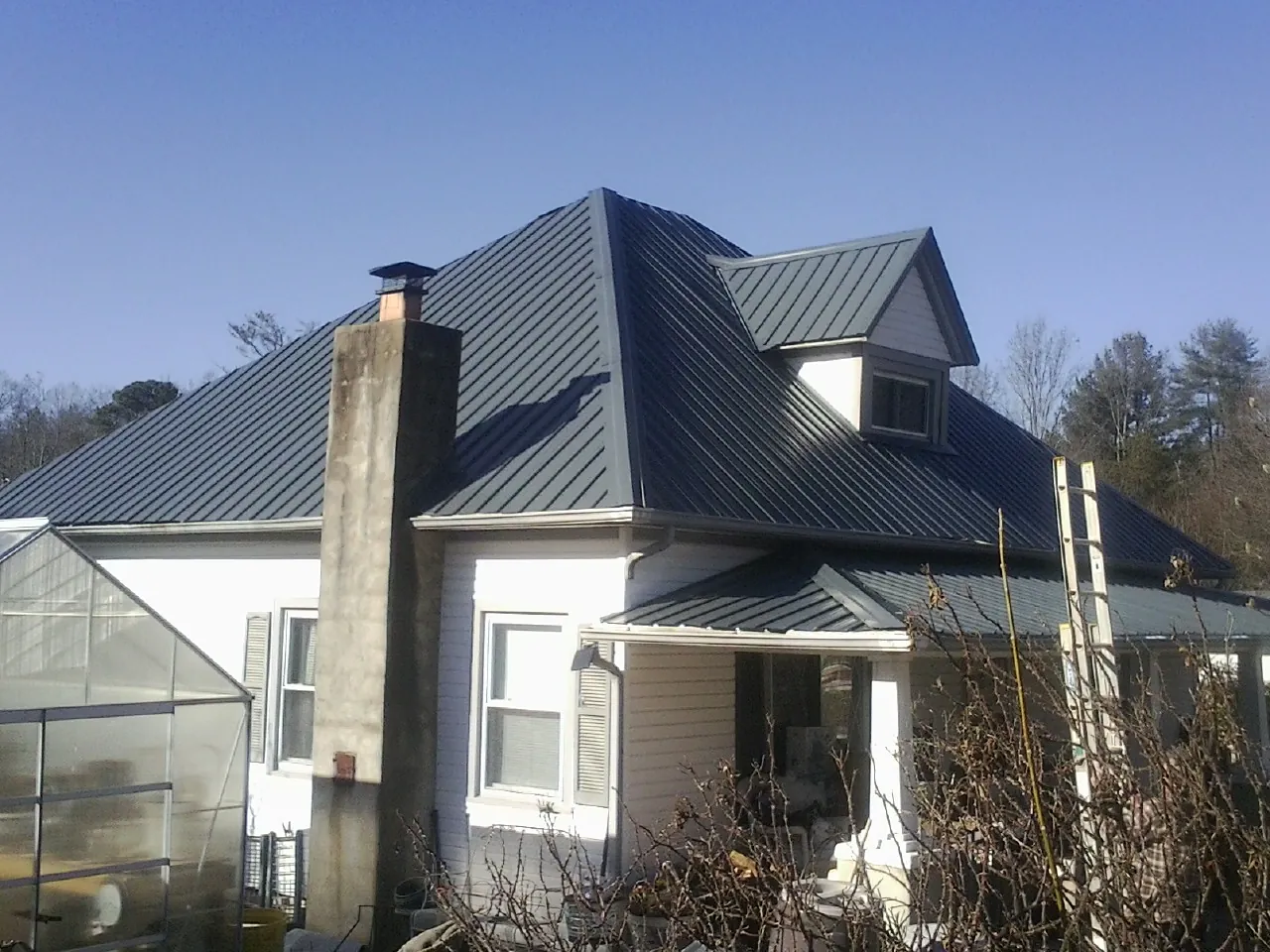 Dark blue standing seam metal roof on a white farmhouse with dormer — Slate & Tile Roof Repair by Roofing Brothers in Tama