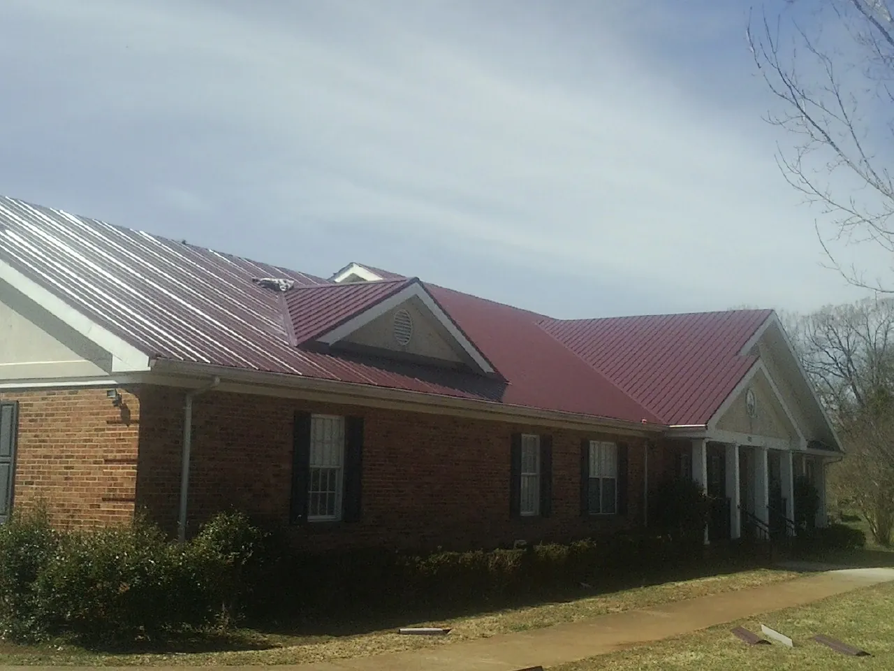 Red metal roof with gabled entries on a long brick building, from a Hail Damage Roof Repair job in Tama