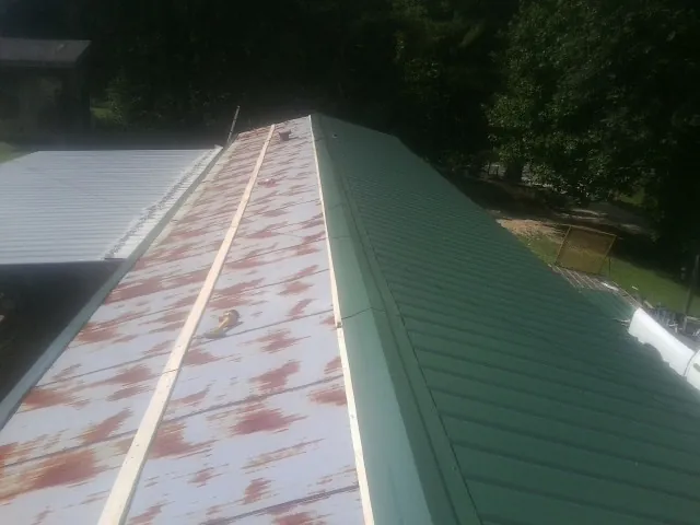 Old rusted panels beside newly installed green metal roofing — Wind Damage Roof Repair by Roofing Brothers in Tama