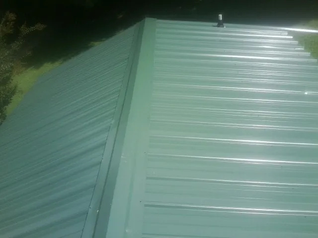 New green metal panels meeting at the ridge of a roof — Flat Roof Repair work by our crew in Tama