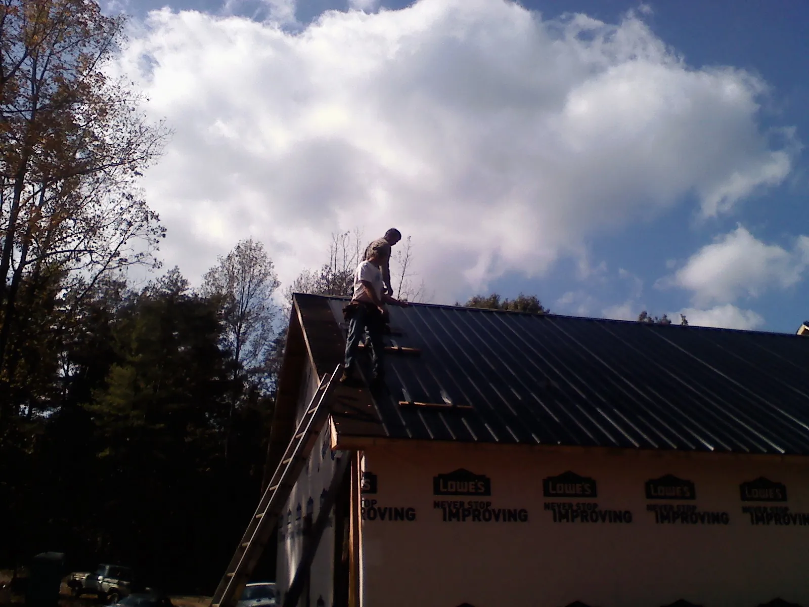Roofer fastening dark metal panels high against a cloudy sky, from a Roof Inspection job in Tama