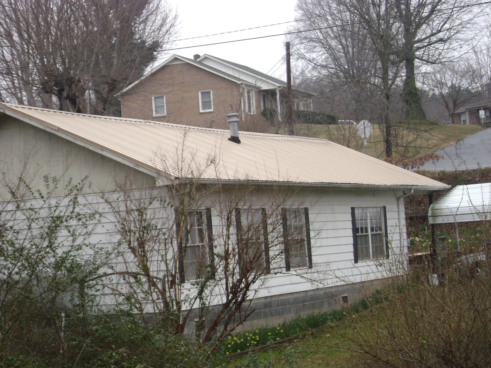 Tan metal roof on a white sided house set into a hillside — Commercial Roofing by Roofing Brothers in Tama