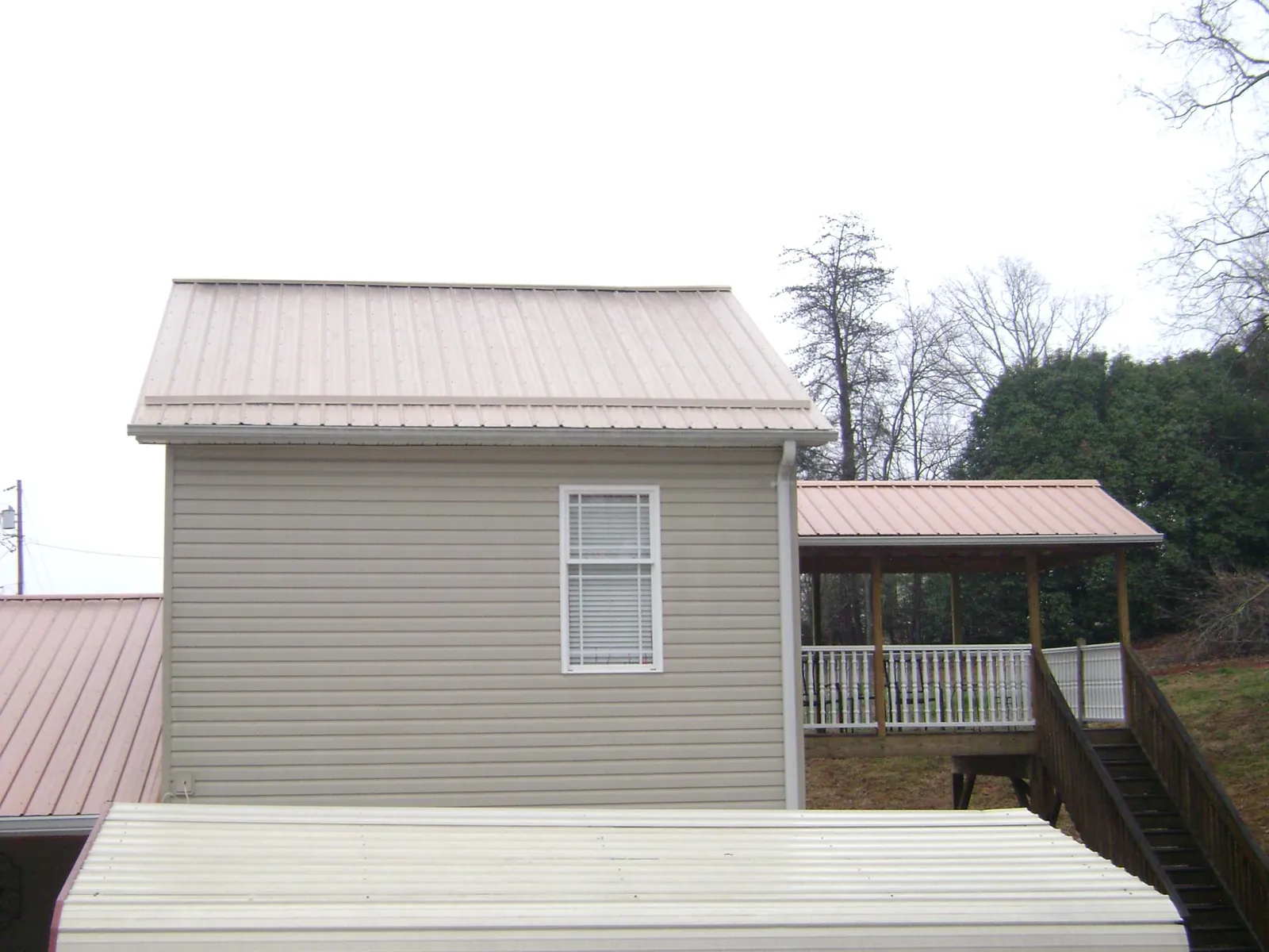 Tan metal roofs on a two story addition and attached porch, from a Roof Replacement job in Tama