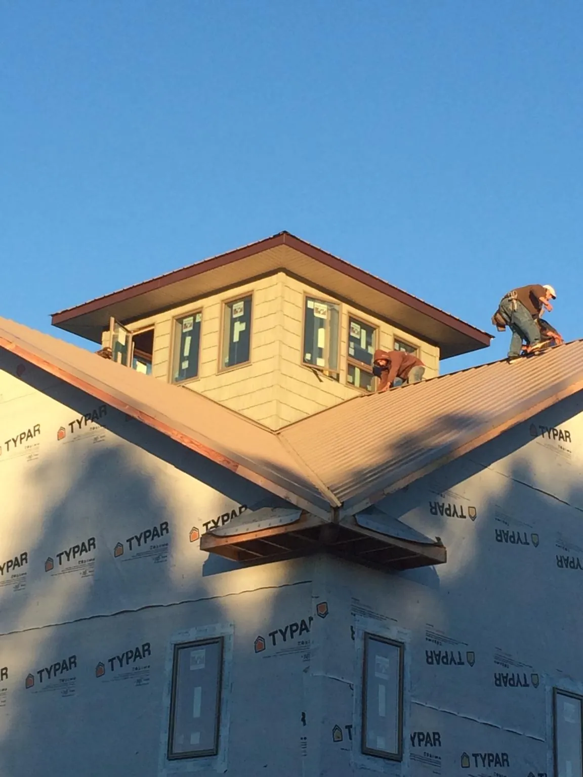 Roofers working around a rooftop cupola on a new metal roof at sunset — Roof Waterproofing in Tama by Roofing Brothers